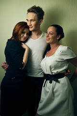 Two women lean to a tall man in white t-shirt