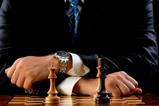 Close Up Man In Suit Playing Carved Wooden Chess Pieces On Board In Check Mate White Winning