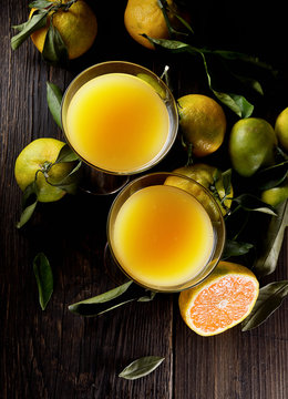 Two Glasses  of fresh tangerine juice with ripe tangerines, leaves and old-fashioned straw on a wooden background