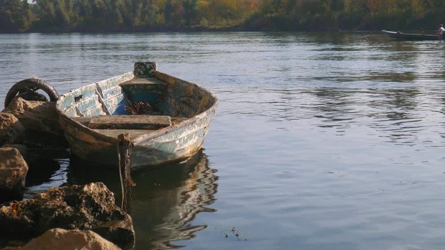 Old moored boat in a river, a newer one goes downstream 

