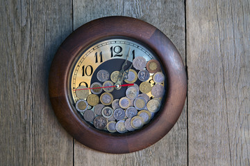 Clock with coins on the wooden background