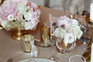 White and pink flowers stand in golden vases on table covered wi