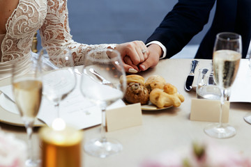 Naklejka na ściany i meble Bride in lace dress holds groom's hand on dinner table
