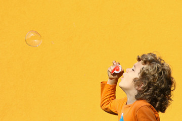 Boy blowing soap bubbles sideview against a yellow wall background