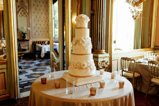 Tall white tired wedding cake stands on the round table in the r