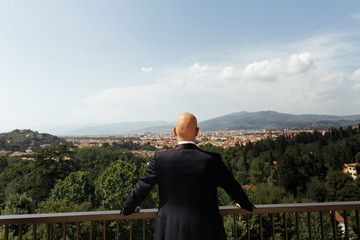 Look from behind at man bending over the balcony while watching