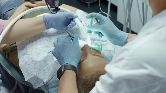 Doctor dentist using dental microscope in dental office for operation of a woman patient
