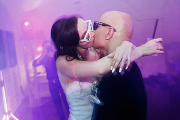 Bride and groom in funny glasses kiss in pink disco lights