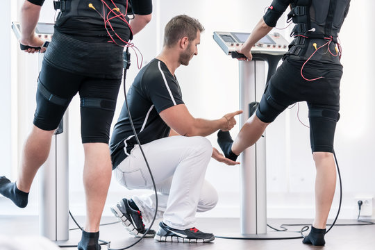 Couple in EMS gym training legs, the trainer is correcting them