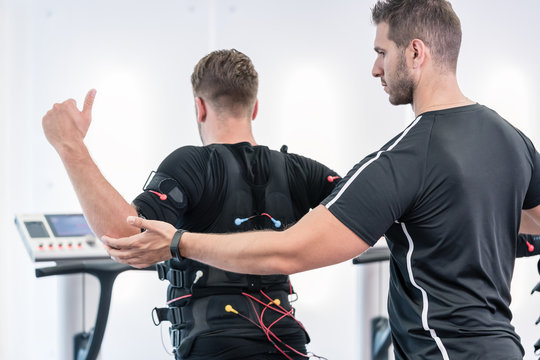 Trainer helping man to do an exercise right in the EMS gym
