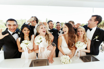 Laughing groomsmen and bridesmaids pose before white bar