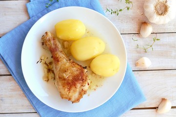 Roasted chicken with fresh garlic, thyme and potatoes on white plate on blue cloth on wooden background