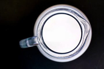 White milk in the glass with the jug on the black background