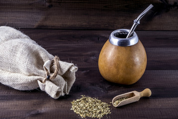 yerba mate with gourd matero, bombila, wooden spoon and linen bag on wooden background.