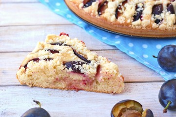 Piece of summer cake with plums on blue cloth on wooden background