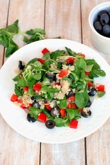 Fresh healthy vegan salad with quinoa, corn salad, black olives, red pepper and olive oil on white plate cloth on white wooden background