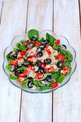 Fresh healthy vegan salad with quinoa, corn salad, black olives, red pepper and olive oil in glass bowl cloth on white wooden background