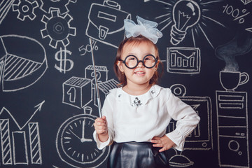 The little smart girl in glasses holding a pointer on dark background with business or school picture