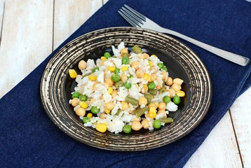 Healthy vegan meal with rice, chickpeas, sweet corn, peas, green beans and rice on dark plate on jeans cloth on wooden background