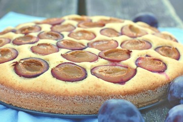 Piece of summer cake with plums on blue cloth on wooden background