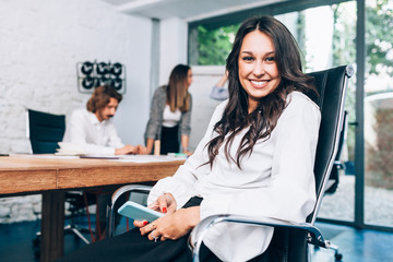 Businesswoman sitting at the office table with smartphone