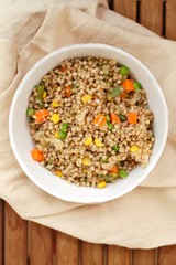 Healthy Czech vegan meal, buckwheat with carrot, sweet corn, peas, green beans and onion in white bowl with fork on the brown cloth