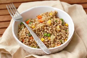 Healthy Czech vegan meal, buckwheat with carrot, sweet corn, peas, green beans and onion in white bowl with fork on the brown cloth