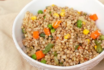Healthy Czech vegan meal, buckwheat with carrot, sweet corn, peas, green beans and onion in white bowl with fork on the brown cloth