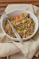 Healthy Czech vegan meal, buckwheat with carrot, sweet corn, peas, green beans and onion in white bowl with fork on the brown cloth