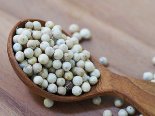 white pepper seeds in wooden spoon on wooden background