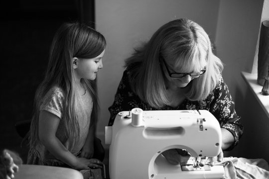 Woman using sewing machine, granddaughter watching her sew, black and white