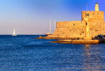 View of the historic Mandraki Harbour with St. Nicholas Fortress before sunset on the Island of Rhodes, Greece