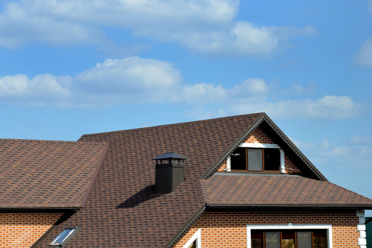 Modern tile roof house with chimneys and Windows against blue sky with clouds.