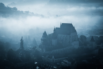 Mysterious misty morning over Biertan village, Transylvania, Romania. Blue colors. spooky,...