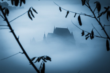 Mysterious misty morning over Biertan village, Transylvania, Romania. Blue colors. spooky,...