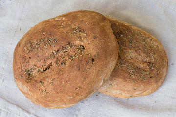 Two loaves of homemade bread lying on the tablecloth. Fresh fragrant bread with aromatic herbs. A whole loaf of bread  on a light background.