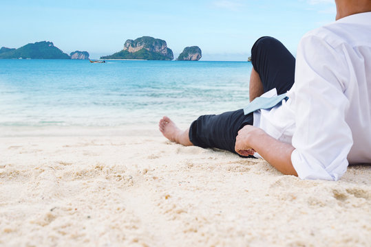Businessman lying relaxing on sand beach look out to sea in holi