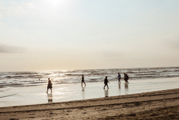 Fototapeta na wymiar Summer beach scene: unrecognizable silhouettes of people walking by seashore on sunset 