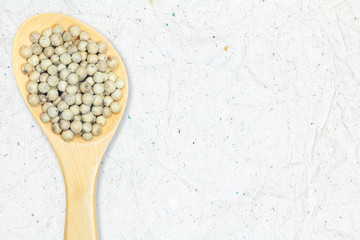 White pepper in wooden spoon on recycled crumpled white paper background for design with copy space for text or image.
