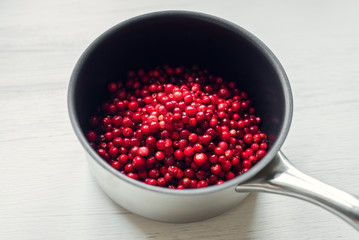 Fresh cranberries in a saucepan on a white wooden table