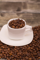 small white cup with coffee beans on wooden background