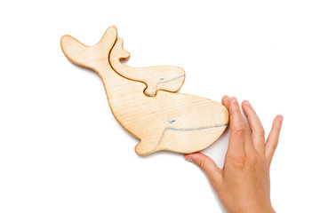 Fototapeta premium Wooden puzzle in the form of a whale and little whale with hands isolated on white.