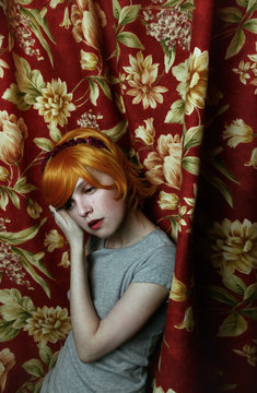 Retrato de una chica pelirroja, triste, escondida tras una cortina antigua 