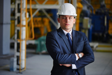 Portrait of a man in a suit and a helmet in the factory building on the background of the industrial equipment