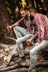 Two friends Lumberjack worker sitting in the forest and drinking beer.Resting after hard work.