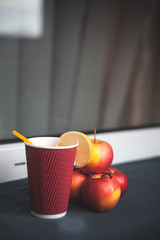 Warm tea with lemon and apples on the table. Red cup with yellow straw
