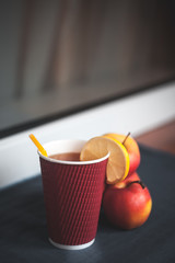 Warm tea with lemon and apples on the table. Red cup with yellow straw