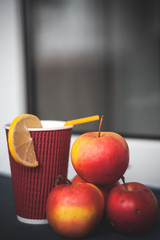 Warm tea with lemon and apples on the table. Red cup with yellow straw
