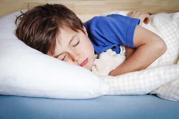 Kind schläft mit Kuscheltier im Bett 