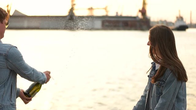 couple opens the champagne on the background of the port.